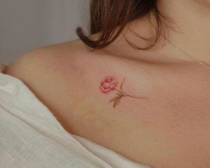 Close up of a red/pink and green peony tattoo on a collarbone